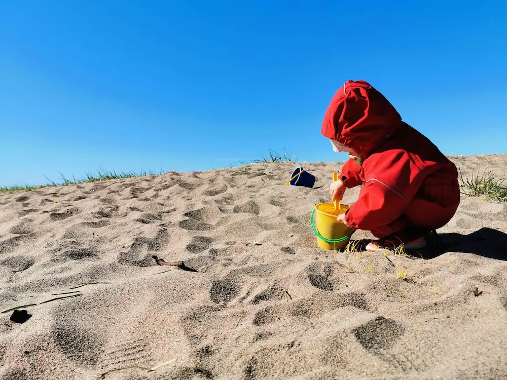Toddler in red hoodie playing in sand