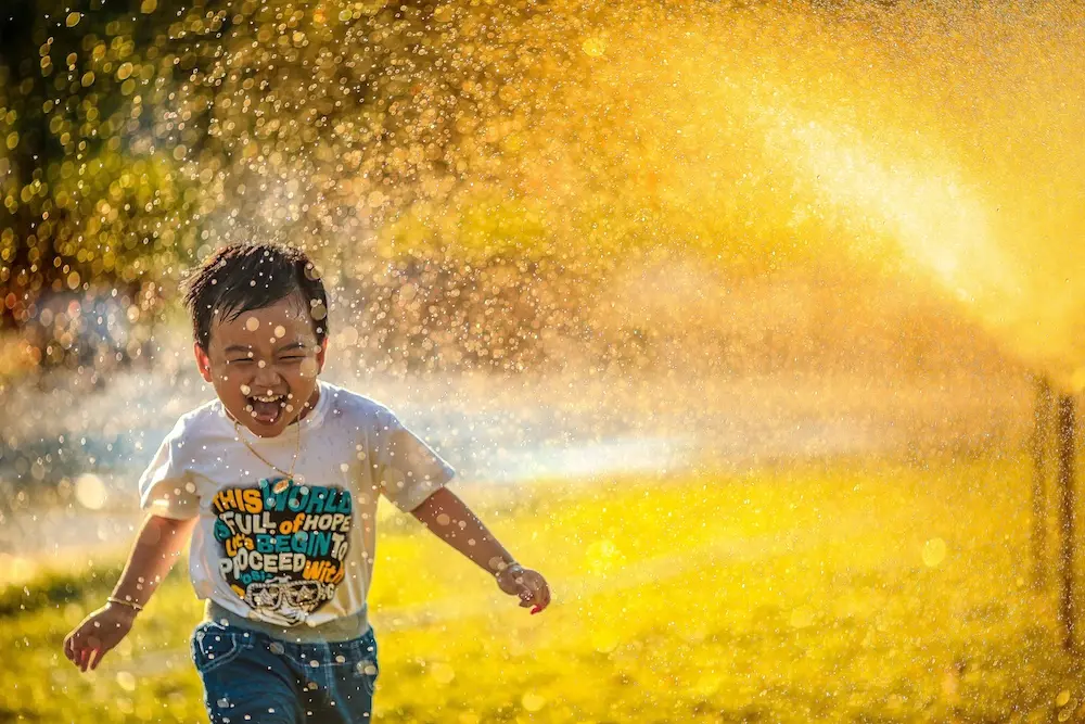 Boy running through a water sprinkler in golden light